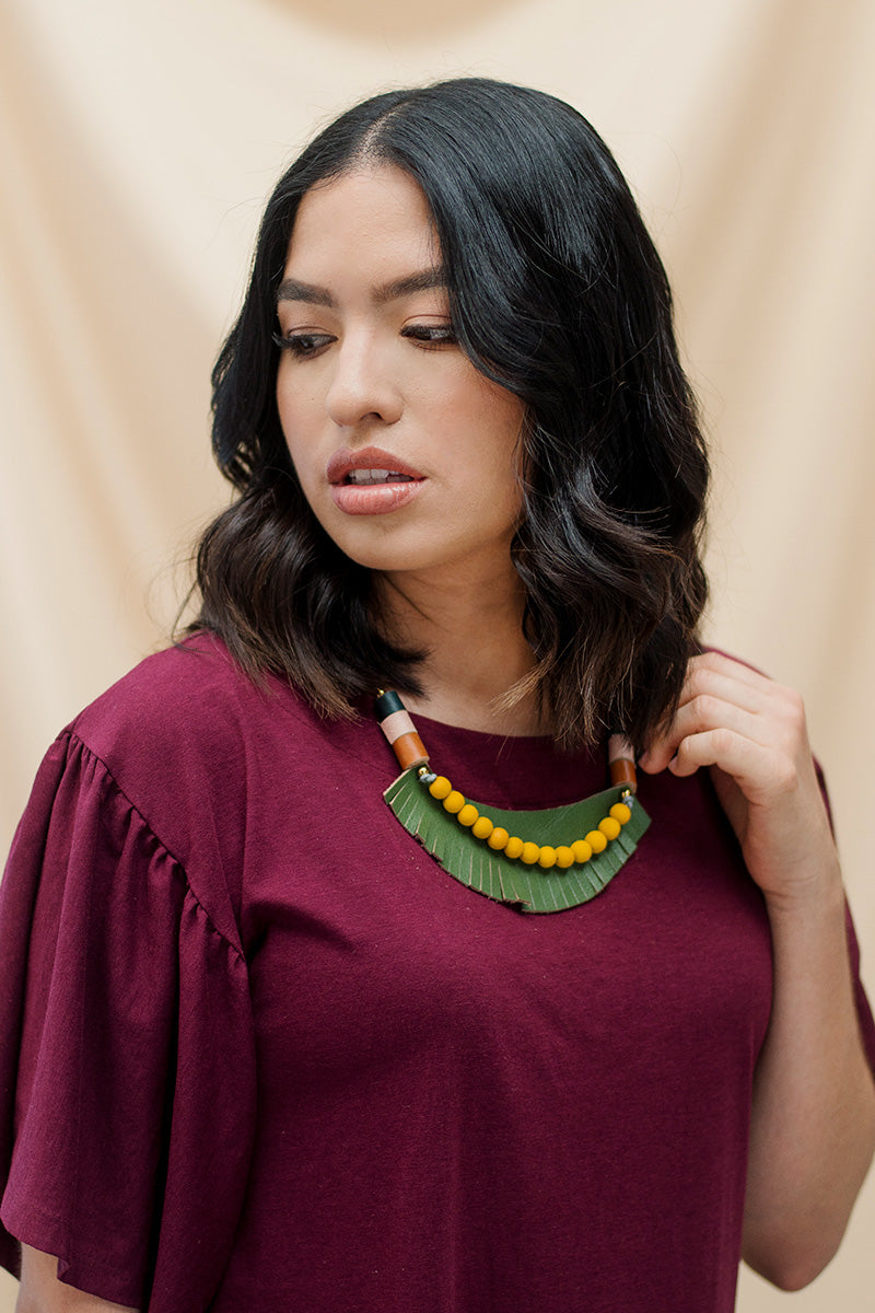 Mujer usando el collar Cleo verde sobre una blusa de color vino