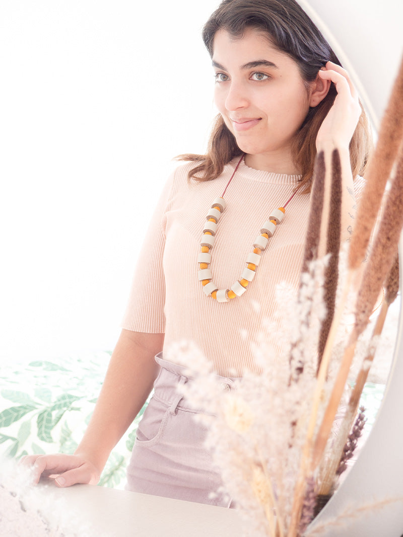 Mujer con blusa salmón usando el collar helena en colores vainilla y amarillo.