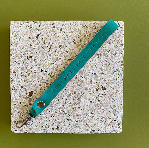 Llavero de cuero en color turquesa oscuro con la frase Reconexión a Tierra estampada a mano