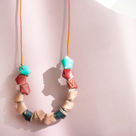 Collar completo hecho con nudos en cuero de colores turquesa, rojo, salmón y verde inglés, cierre ajustable para usarlo corto o largo con cordón de cuero naranja y bolitas doradas de acero inoxidable