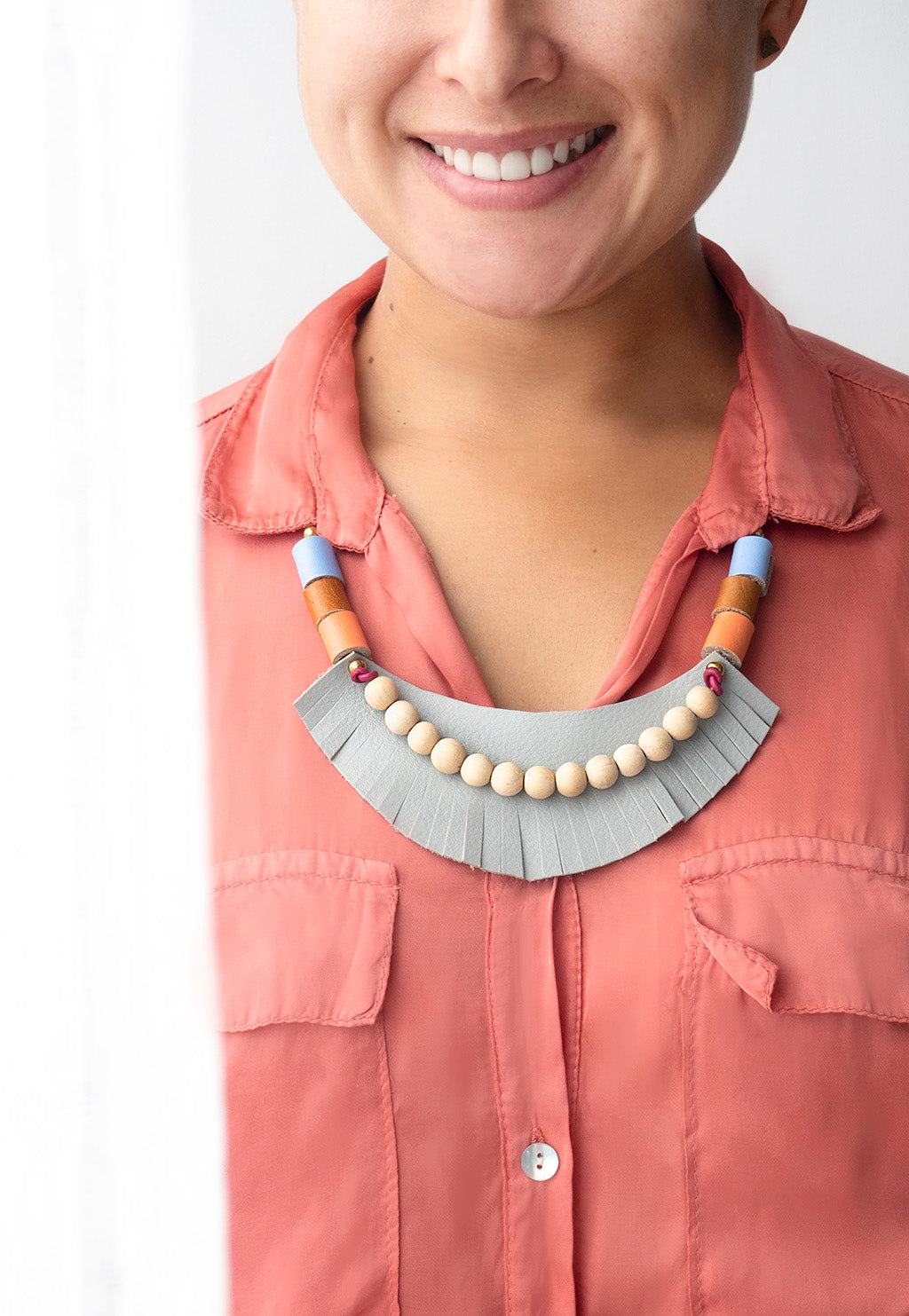 Detalle de mujer sonriente usando el collar gris sobre una blusa de cuello color coral con bolsas a los lados