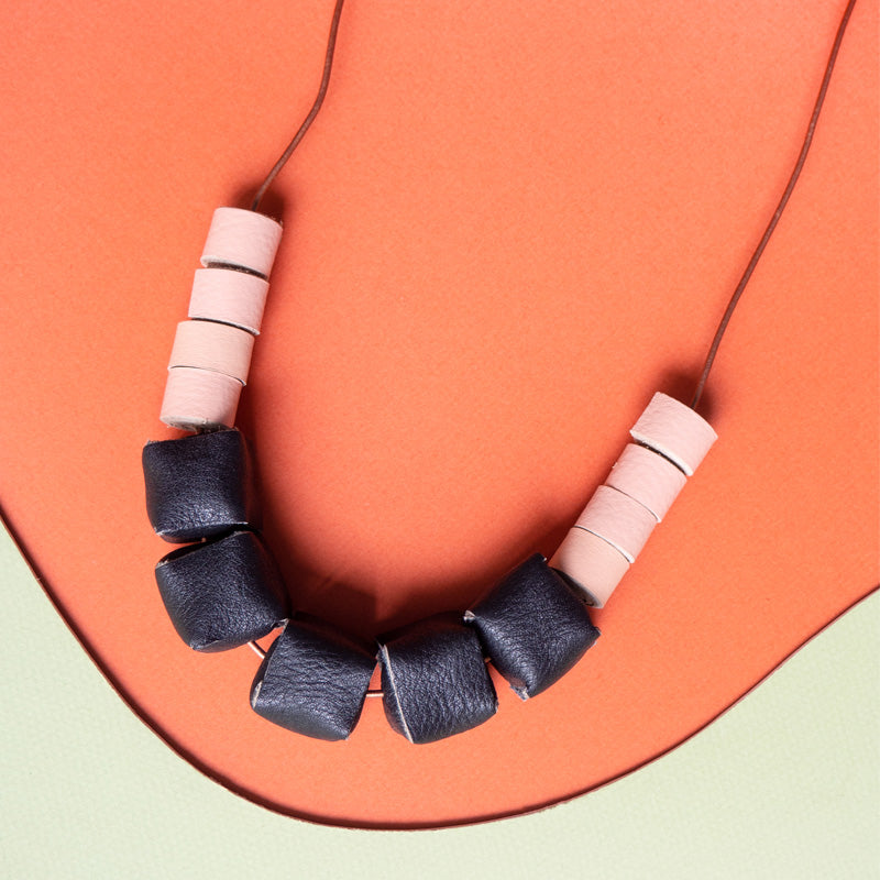 Collar ajustable hecho de retazos de cuero, cubos de color negro y rollitos color salmón con cordón en cuero café