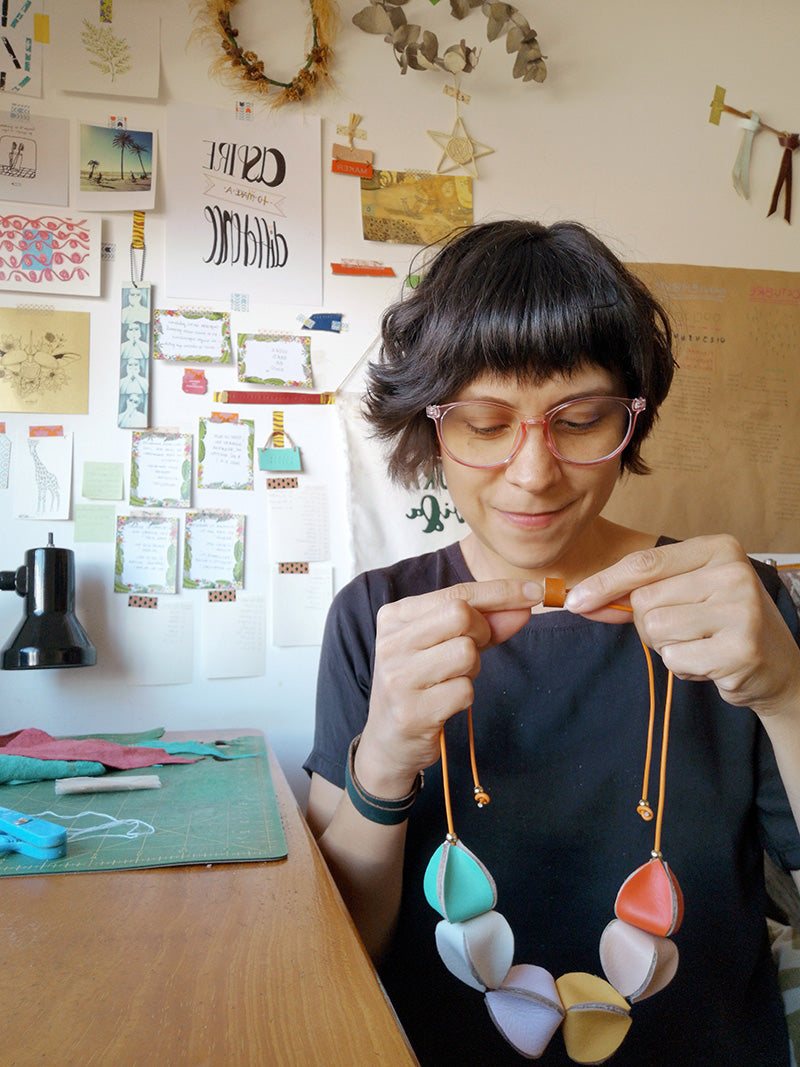 Rebeca Zamora diseñadora de Gato Negro sosteniendo en sus manos el collar Uchuva de cuero de diferentes colores